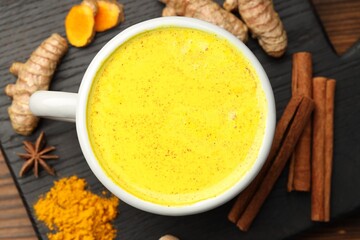 Tasty turmeric latte in cup and spices on wooden table, flat lay