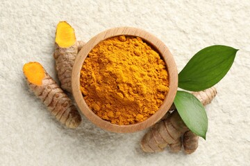 Turmeric powder in bowl, roots and leaves on light textured table, flat lay