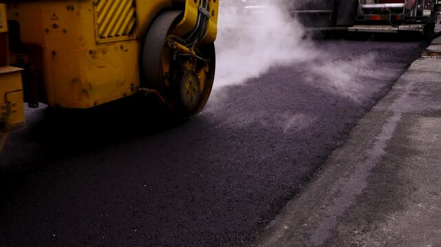 Asphalt Paving. Road Roller Drives Over Hot, Steaming, Freshly Layed Asphalt. Road Roller, Roller-compactor or Roller is a Compactor-type Engineering Vehicle Used to Compact Asphalt.