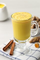 Delicious turmeric latte and rhizomes on white wooden table, closeup