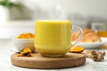 Delicious turmeric latte, powder and rhizomes on white marble table, closeup