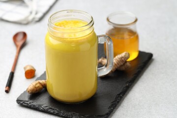 Delicious turmeric latte with honey and rhizomes on grey table, closeup