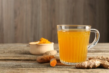Aromatic turmeric tea in glass mug, roots and powder on wooden table, space for text