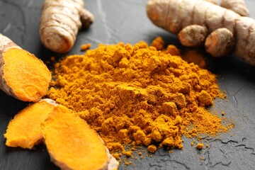 Aromatic turmeric powder and fresh roots on black table, closeup