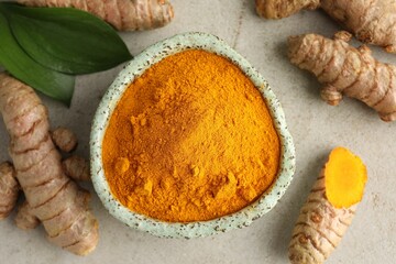 Aromatic turmeric powder in bowl, fresh roots and leaves on light grey table, flat lay