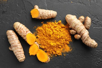 Aromatic turmeric powder and fresh roots on black table, flat lay