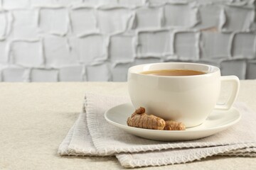Aromatic turmeric tea and rhizomes on white textured table. Space for text