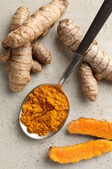 Aromatic turmeric powder in spoon and fresh roots on light grey table, flat lay