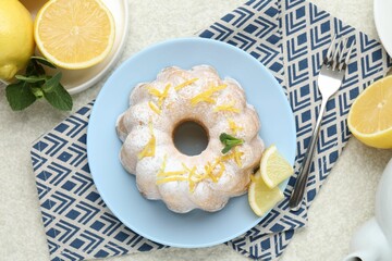 Delicious cake with lemon zest, powdered sugar, mint and citrus fruits on light textured table,...