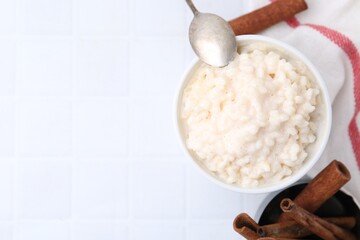 Tasty rice pudding with cinnamon served on white tiled table, flat lay. Space for text