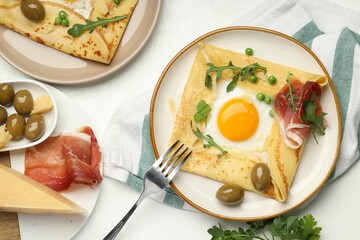 Delicious crepes with egg, bacon, olives and arugula on white table, flat lay