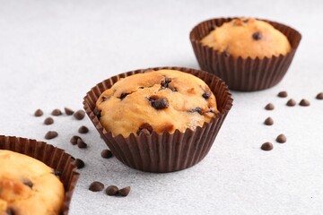 Delicious muffin with chocolate chips on light grey table, closeup