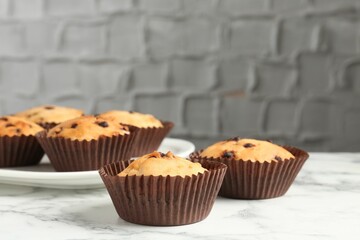 Delicious muffin with chocolate chips on white marble table, closeup