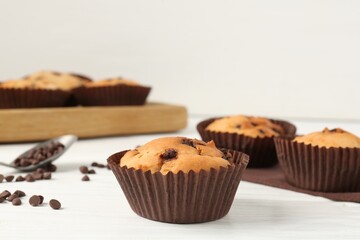 Delicious muffin with chocolate chips on white wooden table, closeup