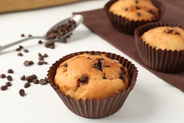 Delicious muffin with chocolate chips on white wooden table, closeup