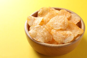 Tasty potato chips in bowl on yellow background, closeup. Space for text