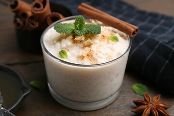 Tasty rice pudding with cinnamon, mint and nuts on wooden table, closeup