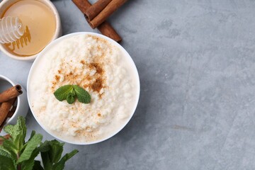 Tasty rice pudding with cinnamon, mint and honey on light grey table, flat lay. Space for text