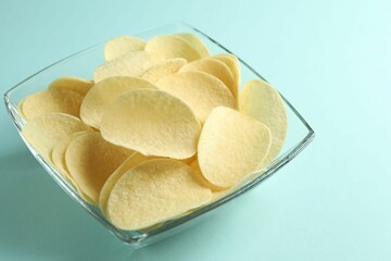 Tasty potato chips on light blue background, closeup