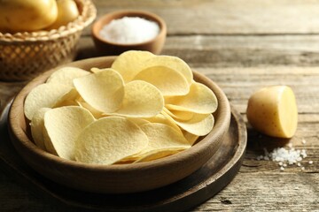 Tasty chips, salt and raw potatoes on wooden table, closeup