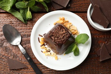 Tasty pudding with peanuts, mint and pieces of chocolate served on wooden table, flat lay