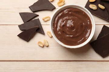 Tasty pudding, pieces of chocolate and peanuts on white wooden table, flat lay