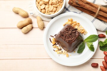Tasty chocolate pudding with peanuts and mint on white wooden table, flat lay