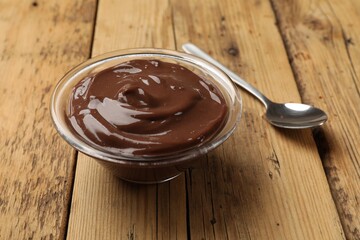 Delicious chocolate mousse in glass bowl and spoon on wooden table, closeup