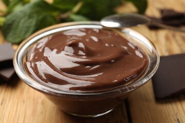 Delicious chocolate mousse in glass bowl and spoon on wooden table, closeup