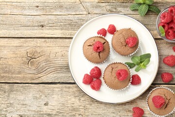 Delicious muffins with raspberries and mint on wooden table, flat lay. Space for text