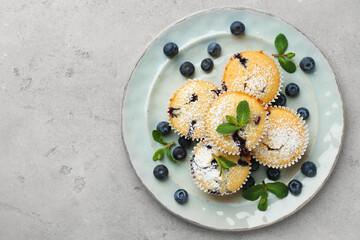 Delicious muffins with blueberries, powdered sugar and mint on grey textured table, top view. Space for text