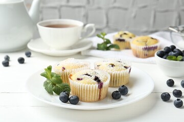 Delicious muffins with blueberries, powdered sugar and mint on white wooden table, closeup