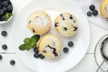 Delicious muffins with blueberries, powdered sugar and mint on white wooden table, flat lay