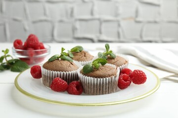 Delicious muffins with raspberries and mint on white wooden table against grey textured background, closeup