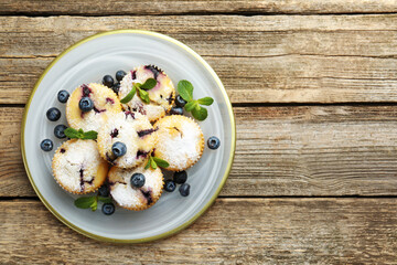 Delicious muffins with blueberries, powdered sugar and mint on wooden table, top view. Space for text