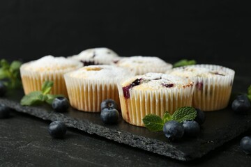 Delicious muffins with blueberries, powdered sugar and mint on dark textured table, closeup