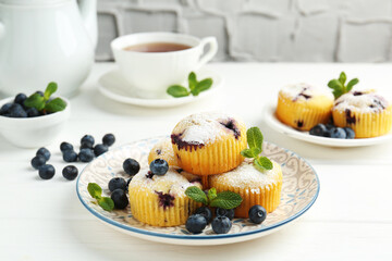 Delicious muffins with blueberries, powdered sugar and mint on white wooden table, closeup