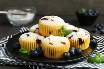 Delicious muffins with blueberries, powdered sugar and mint on dark table, closeup
