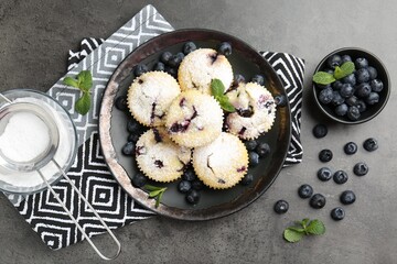 Delicious muffins with blueberries, powdered sugar and mint on dark textured table, flat lay