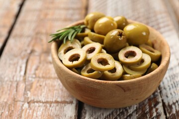 Delicious marinated olive rings, rosemary and whole ones in bowl on wooden table, closeup