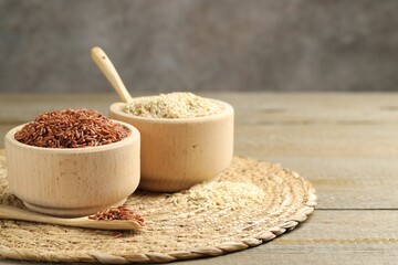 Different sorts of raw brown rice on wooden table against grey background, closeup. Space for text