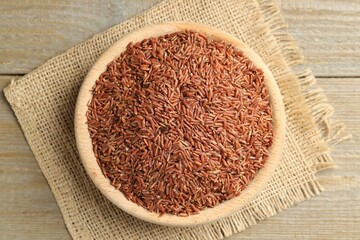 Raw brown rice in bowl on wooden table, top view