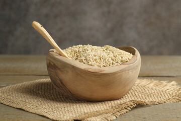 Raw brown rice in bowl on wooden table against grey background, closeup