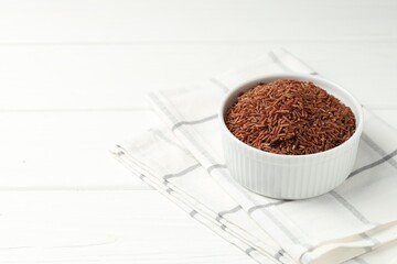 Raw brown rice in bowl on white wooden table, closeup. Space for text