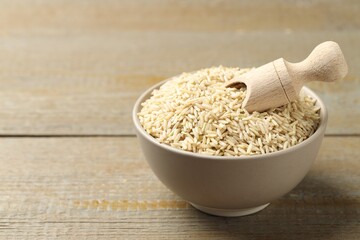Raw brown rice and scoop in bowl on wooden table, closeup. Space for text