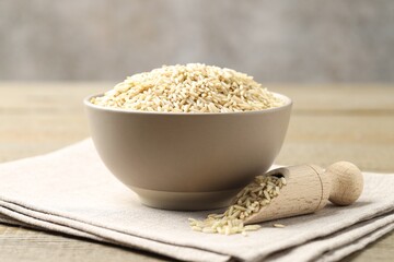 Raw brown rice in bowl and scoop on wooden table against grey background, closeup