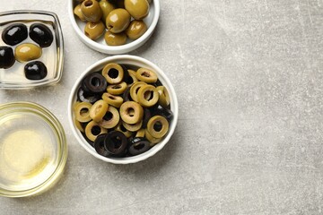 Different delicious marinated olive rings, whole ones and oil on grey textured table, flat lay. Space for text