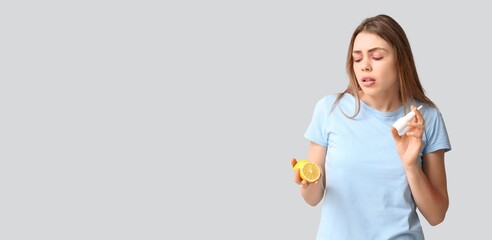 Young woman with lemon and nasal spray suffering from allergy on grey background with space for text