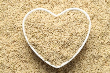 Pile of brown rice with heart shaped bowl, top view