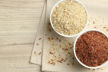 Different types of brown rice in bowls on wooden table, flat lay. Space for text